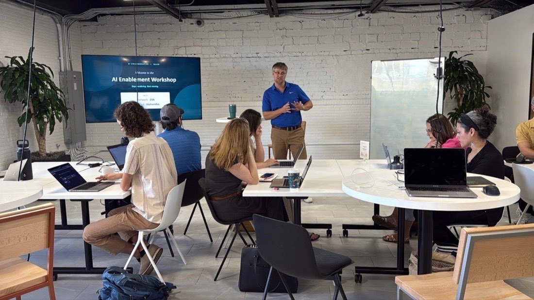 Wide view of the workshop room with attendees at tables and a guide at the front
